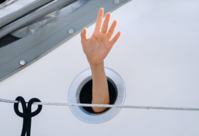 A man's hand sticks out of the porthole window on a ship at sea