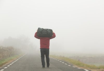 carrying-suitcase-his-arms-unrecognizable-man-walking-along-road-foggy-day