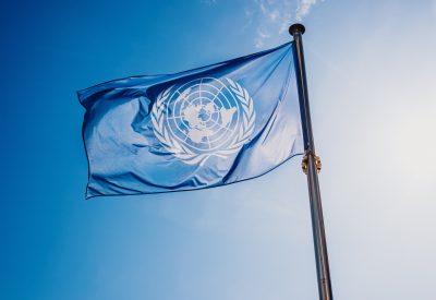 UN flag waved against the sun and blue sky.